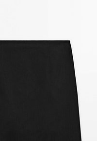 Gros plan sur la partie supérieure d'une jupe crayon noire avec des coutures discrètes sur un fond blanc uni.