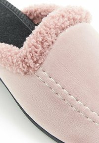 Ciabatta rosa con un morbido collare peloso, una parte superiore in camoscio liscio e cuciture bianche a contrasto. Suola nera alla base.