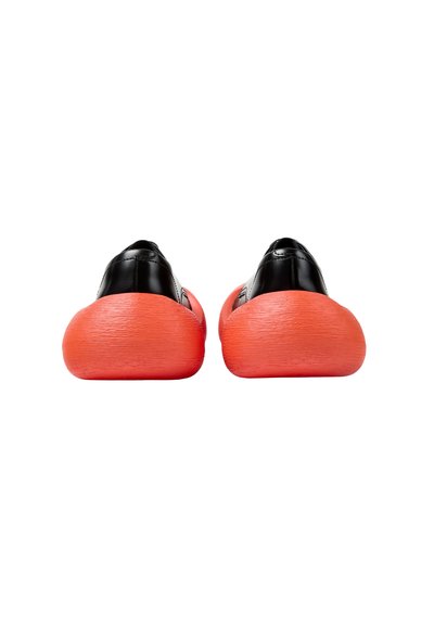 Paire de chaussures noires formelles avec des semelles épaisses texturées rouges vives, vues de dos sur un fond blanc.