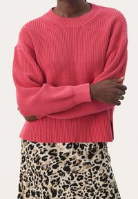 Jasnoróżowy sweter dzianinowy z opadającymi ramionami i ściągaczami, w połączeniu z spódnicą w leopardzi wzór z beżowym i czarnym motywem.