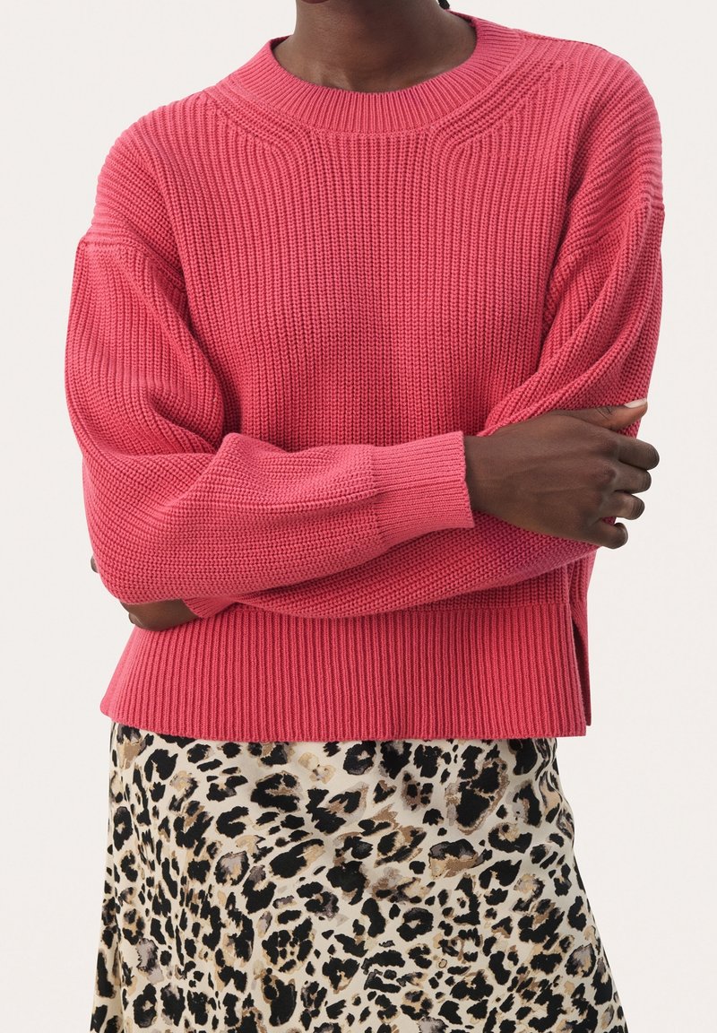 Jasnoróżowy sweter dzianinowy z opadającymi ramionami i ściągaczami, w połączeniu z spódnicą w leopardzi wzór z beżowym i czarnym motywem.