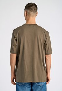 Camiseta de algodón verde oliva con mangas cortas, cuello redondo y corte relajado, vista desde la parte de atrás, combinada con jeans de denim azul.