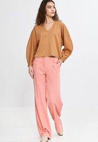 Brązowy top w serek z balonowymi rękawami, w połączeniu z różowymi spodniami o wysokim stanie i szerokich nogawkach, które mają dwa przednie guziki. Miękka, gładka faktura.