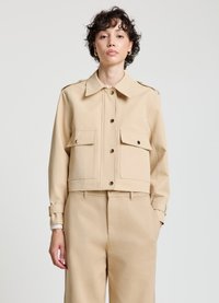 Beige kurze Jacke mit Kragen, zwei Fronttaschen und Knopfverschluss. Kombiniert mit beigen Hosen mit glatter Textur.