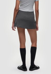 Gonna mini grigia con un design sartoriale, pieghe frontali piatte, abbinata a calze nere al ginocchio e scarpe nere lucide.