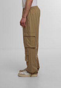 Beige cargo bukser med elastisk talje, to sidelommer og to store cargo lommer på lårerne. Stofblanding af bomuld.