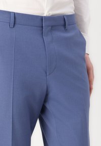 Light blue tailored trousers made of smooth fabric, featuring a flat front, side pockets, and a fitted waist.