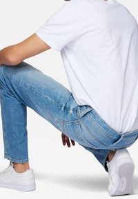 Vaqueros de denim azul claro con corte slim, diseño estándar de cinco bolsillos y un ligero desvanecimiento. Combinados con una camiseta blanca lisa y zapatillas blancas.
