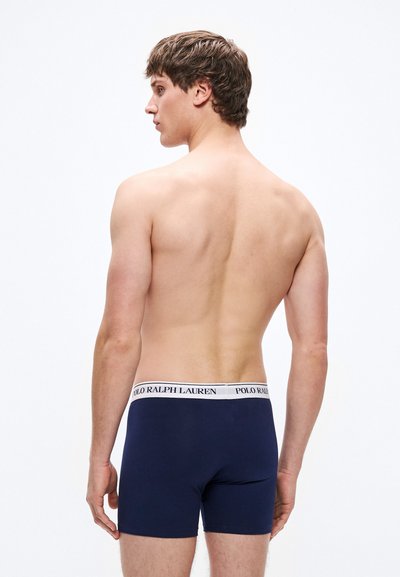 Temno modre bokser hlačke z belim elastičnim pasom z besedilom "POLO RALPH LAUREN"; prilegajoč se kroj in gladka tekstura, prikazane od zadaj.