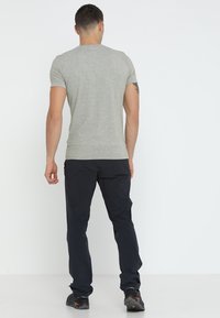 Maglietta grigia con texture abbinata a pantaloni blu scuri. L'outfit è completato da robusti scarponi neri con dettagli arancioni.