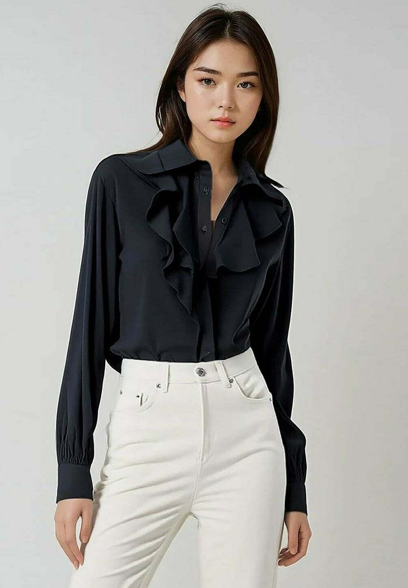 Blouse noire avec volants et boutons sur le devant, manches longues, associée à un pantalon blanc taille haute. Tissu lisse, coupe ajustée.