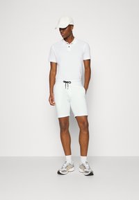 White polo shirt with two-button placket, light blue shorts with drawstring, and silver athletic shoes with accents. White cap worn.
