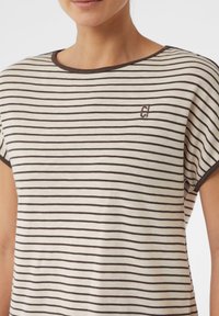 Gestreiftes T-Shirt in Creme- und Brauntönen mit rundem Ausschnitt und kurzen Ärmeln. Kleines Logo-Detail am Kragen. Weiche Textur.