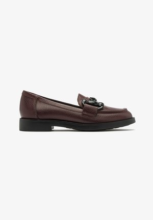 Mocassins en cuir bordeaux avec une finition texturée, présentant une sangle à l'avant et un accent en métal noir rond. Semelle en caoutchouc noir solide et basse.