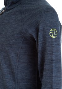 Tummansininen vetoketjullinen takki, joka on valmistettu teksturoidusta kankaasta. Takissa on keltainen logo vasemmassa olkapäässä ja näkyviä saumurivaihtoehtoja.