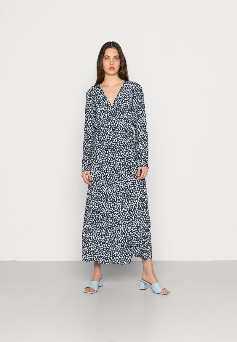 Vestido longo azul-marinho com padrão floral, decote em V e mangas compridas. Acompanhado por sandálias de salto bloco azul claro. Textura suave.