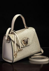 Bolso estructurado beige con una superficie texturizada y brillante, herrajes de metal dorado y un cierre decorativo en forma de cabeza de leopardo. Incluye una correa desmontable.