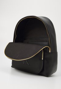 Rucsac din piele neagră cu fermoar aurit, interior spatios, buzunar plat și vârf rotunjit, având logo-ul embosat pe partea din față.