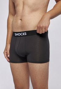 Schwarze Boxershorts aus einem glatten, dehnbaren Material. Mit einem breiten, elastischen Bund mit dem weißen "SNOCKS"-Logo.