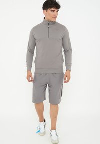 Grå atletisk zip-up-tröja med ståkrage, tillsammans med grå cargoshorts. Mjuk kvalitet, ribbade ärmslut och texturerat mönster på tröjan.