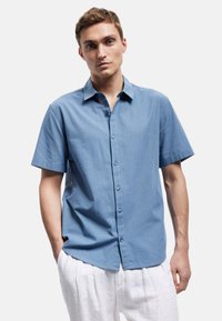 Lichtblauw kort-lang mouw button-up shirt met een kraag, gestructureerde stof, knopen aan de voorkant en een relaxed fit, gecombineerd met witte broeken.