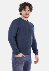 Maglione lavorato a maglia blu navy con scollo rotondo e texture a coste. Presenta maniche lunghe e un logo discreto sul petto.