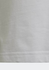 Zbliżenie na biały materiał z widocznym szwem wzdłuż dolnej krawędzi, ukazującym teksturę i szczegóły obszycia.