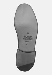 Semelle de chaussure en cuir noir avec un logo en relief. Présente une surface lisse, une forme arrondie et des rivets en métal sur le talon pour le renforcement.