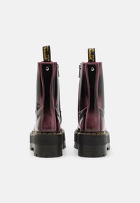Černé a burgundské kotníkové boty s lesklým povrchem, kontrastním prošíváním a silnou černou platformou. Vybaveny žlutým poutkem.