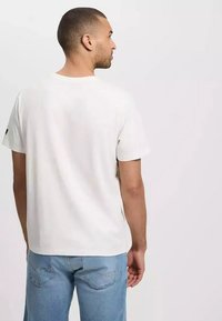 Biała koszulka z krótkim rękawem wykonana z bawełny, z okrągłym dekoltem i luźnym krojem. Połączona z jasnoniebieskimi dżinsami z tylnymi kieszeniami.