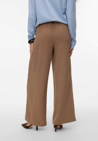 Pantalon à jambes larges en tissu léger de couleur marron clair avec une finition texturée ; associé à un haut bleu à manches longues. Pas d’éléments métalliques visibles.