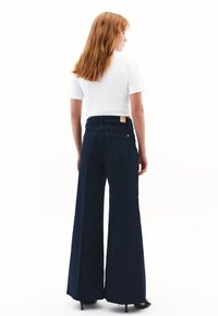 Szerokie, ciemnoniebieskie dżinsy z wysokim stanem, z tylnymi kieszeniami i skórzaną metką na pasku, w komplecie z prostą białą bluzką.