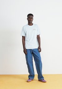 Világoskék, rövid ujjú póló, kis "Dickies" logóval a mellkason, kék farmernadrággal és lila slip-on cipővel párosítva.