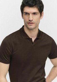 Bruine polo-shirt van geweven katoen. Heeft een klassieke kraag en korte mouwen. Eenvoudig ontwerp met een voorste knoopsluiting.