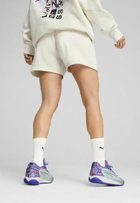 Sudadera beige claro y pantalones cortos, zapatillas con patrón morado y azul, calcetines blancos con logo negro, corte relajado, texturas suaves.