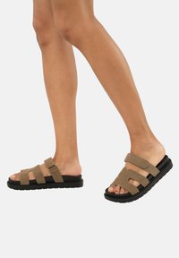 Sandali in suede marrone con tre cinturini, fibbia regolabile e suole in gomma. Design open-toe che mette in mostra i piedi nudi.