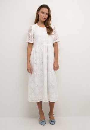 Robe midi blanche en dentelle avec des manches courtes, motif floral, silhouette en A, encolure ronde, associée à des chaussures bleu clair avec un détail en nœud.