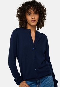 Cardigan en tricot bleu marine avec un col rond, fermeture par boutons et manches longues. Fabriqué à partir d'un matériau doux avec une texture lisse.