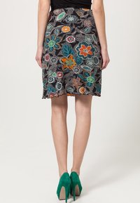 Zwarte bloemenrok met kleurrijke geborduurde bloemen en bladeren. De zoom is gegolfd en de rok is gecombineerd met groene hoge hakken.