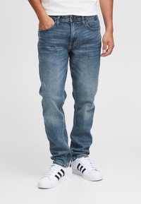 Jeans i denim med en mellanmörk blå nyans, med rak benpassform, fem fickor och subtil blekning. Kombineras med vita sneakers med svarta ränder.