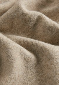 Jasno beżowy materiał o miękkiej, teksturowanej dzianinie, z delikatnymi fałdami i ciepłym wyglądem.