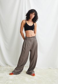 Zwarte cropped beha gecombineerd met hooggetailleerde, wijduitlopende grijze broek. Model draagt rood-gele schoenen. Glad materiaal en comfortabele pasvorm.