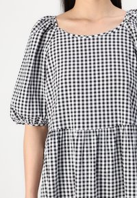 Vestido xadrez em preto e branco com mangas bufantes, decote em forma de canoa, bainha em camadas de babados e tecido de algodão texturizado.