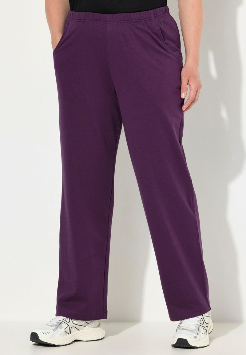 Pantalons violets à taille élastique avec poches latérales, fabriqués en tissu doux, avec une coupe droite et portés avec des chaussures de sport blanches.