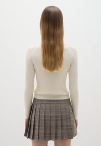 Maglione beige a coste con maniche lunghe abbinato a una gonna plissettata a quadri marrone con accenti arancioni. La texture è liscia, con un design aderente.
