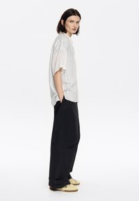 White striped short-sleeve shirt, loose-fitting black pants, and light yellow sneakers. Side view, showcasing relaxed design and silhouette.