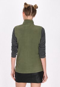 Gilet in pile verde con colletto alto e maniche lunghe grigie, dotato di una texture liscia e di un orlo abbassato. Gonna mini nera in fondo.