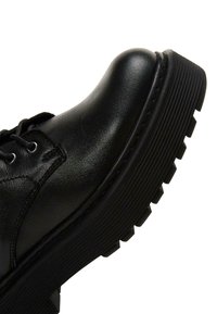 Scarpa di pelle nera con punta arrotondata, design con lacci e suola in gomma spessa e scanalata. Texture liscia con dettagli di cucitura discreti.
