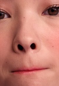 Gros plan d'un visage montrant un teint lisse, un nez proéminent, des yeux marron et une coloration subtile des lèvres, avec une texture minimale visible.
