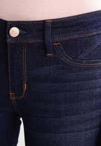 Mörkblå denimjeans med orange sömmar, med en metallknapp stängning, framfickor och en slät yta.